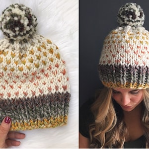 May include: A white knit beanie with a brown, white, and green pom pom. The beanie has a brown, white, and yellow stripe at the bottom.