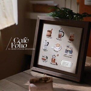 Puede incluir: Una obra de arte enmarcada con ilustraciones temáticas de café. La obra incluye imágenes de granos de café, una prensa francesa, una Chemex, una cafetera italiana, un capuchino, una máquina de espresso, una cafetera de goteo y un molinillo de café. El marco tiene un acabado marrón oscuro.