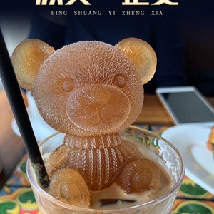 May include: A glass of iced coffee with a brown teddy bear ice cube. The text "冰球一首歌" is written in gold on a black background above the coffee.