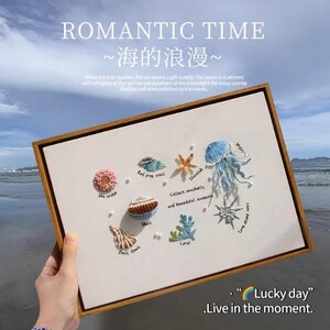 May include: Embroidered artwork in a wooden frame featuring sea creatures like a jellyfish, starfish, and shells. The text "ROMANTIC TIME" and "Lucky day" are visible. The artwork is set against a beach backdrop.