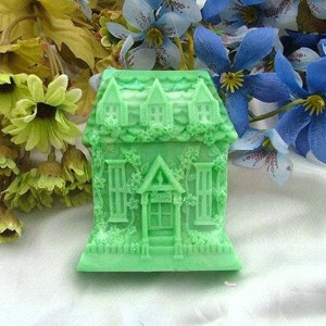 May include: A green detailed house-shaped silicone mold for baking or crafting. The mold has a detailed design of a house with windows, a door, and vines.