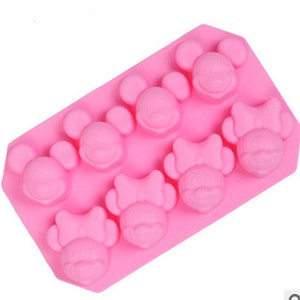 Pode incluir: Forma de silicone rosa com oito cavidades em forma de personagens de desenhos animados com laços e orelhas.