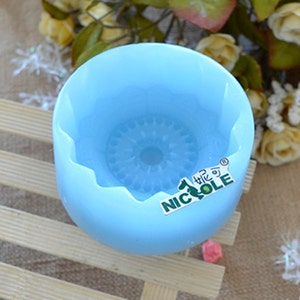 Puede incluir: Un molde de silicona azul claro con un dise&ntilde;o decorativo en el centro. El molde tiene un borde festoneado y las palabras "Nicole" y un logotipo est&aacute;n impresas en el lateral.