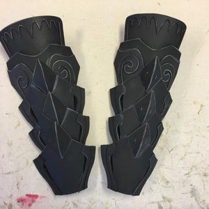 May include: Two black foam pieces with intricate designs, resembling armor or costume pieces.