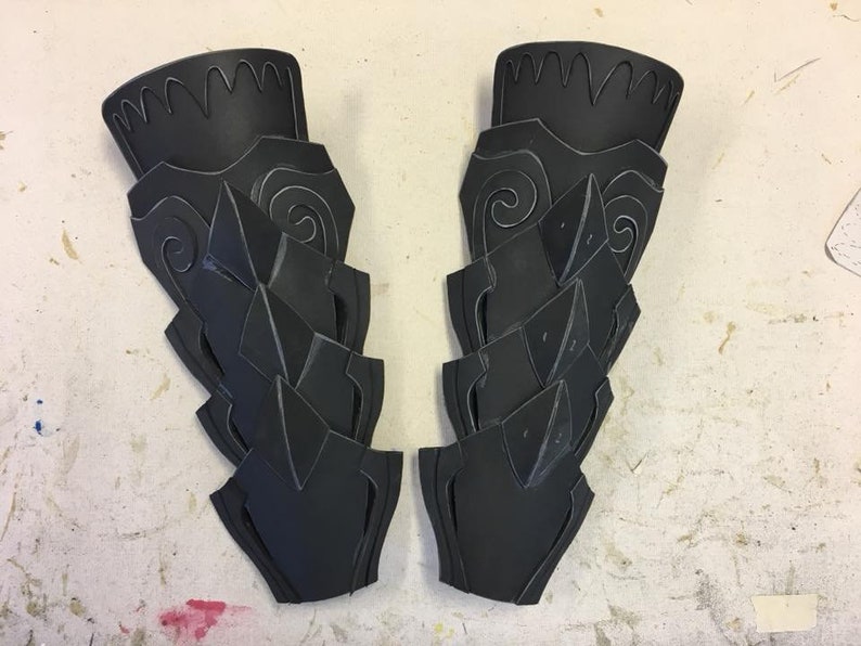 May include: Two black foam pieces with intricate designs, resembling armor or costume pieces.
