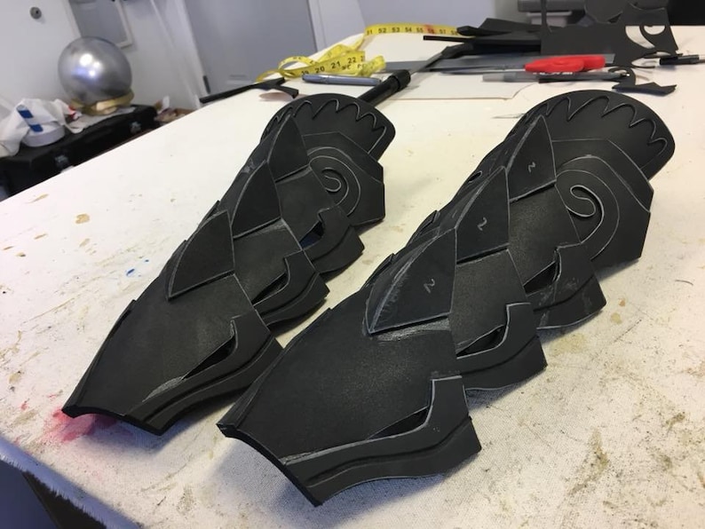 May include: Black foam pieces with cutouts, resembling armor or a costume, laid out on a white surface. The pieces are numbered 1 and 2.