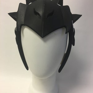 May include: Black foam headpiece with a pointed, spiky design. The headpiece has two eye holes and is worn on a white mannequin head.