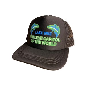 Op de afbeelding: Zwarte truckerpet met een mesh achterkant en een gebogen klep. De voorkant toont de tekst "LAKE ERIE WALLEYE CAPITAL OF THE WORLD" in blauw en groen, en twee gestileerde vissen.