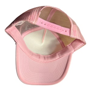 Pode incluir: Bon&eacute; de caminhoneiro de malha rosa com uma al&ccedil;a ajust&aacute;vel branca. O bon&eacute; &eacute; feito de um material de malha respir&aacute;vel e tem um painel frontal rosa s&oacute;lido.