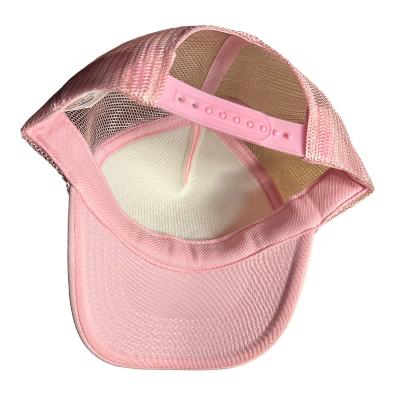 Pode incluir: Bon&eacute; de caminhoneiro de malha rosa com uma al&ccedil;a ajust&aacute;vel branca. O bon&eacute; &eacute; feito de um material de malha respir&aacute;vel e tem um painel frontal rosa s&oacute;lido.