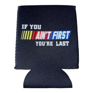 Pu&ograve; includere: Isolante per bevande nero con il testo bianco "IF YOU AIN'T FIRST YOU'RE LAST". Le parole "AIN'T FIRST" sono in un design colorato con strisce gialle, rosse e blu. L'isolante ha un fondo curvo per contenere una bevanda.