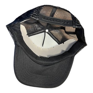 May include: Black mesh trucker hat with a black adjustable strap and a white mesh panel. The hat is turned inside out to show the interior.