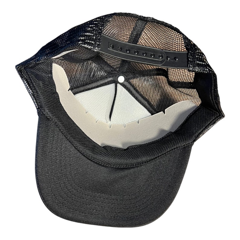 May include: Black mesh trucker hat with a black adjustable strap and a white mesh panel. The hat is turned inside out to show the interior.