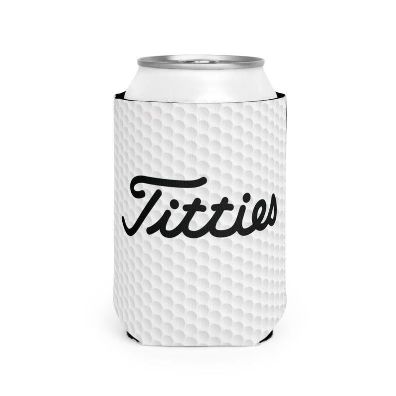May include: White golf ball patterned can cooler with the word "Titties" in black cursive lettering.