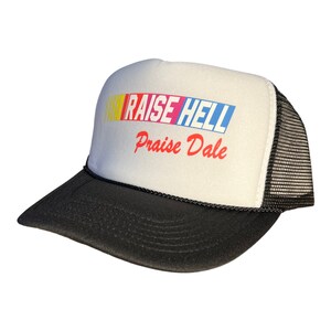 Op de afbeelding: Een witte trucker-pet met een zwart mesh-achterpaneel. De voorkant van de pet heeft een kleurrijk race-streepontwerp en de tekst "RAISE HELL Praise Dale".