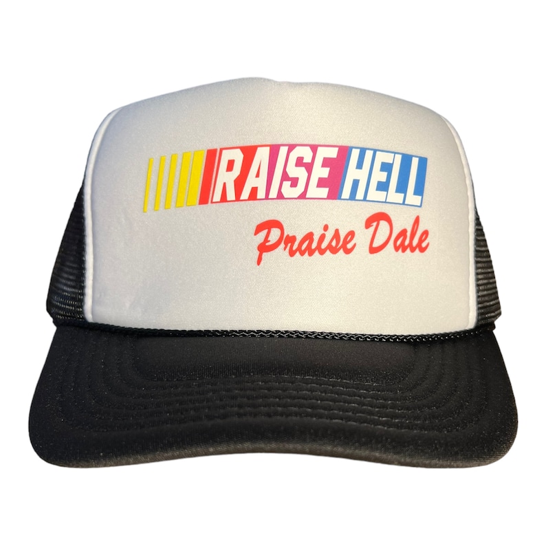 Op de afbeelding: Een witte truckercap met een zwart mesh achterpaneel. De voorkant van de cap heeft een kleurrijk race-streepontwerp met de tekst "RAISE HELL" in rood, blauw en geel. Onder de streep staat de tekst "Praise Dale" in rood.