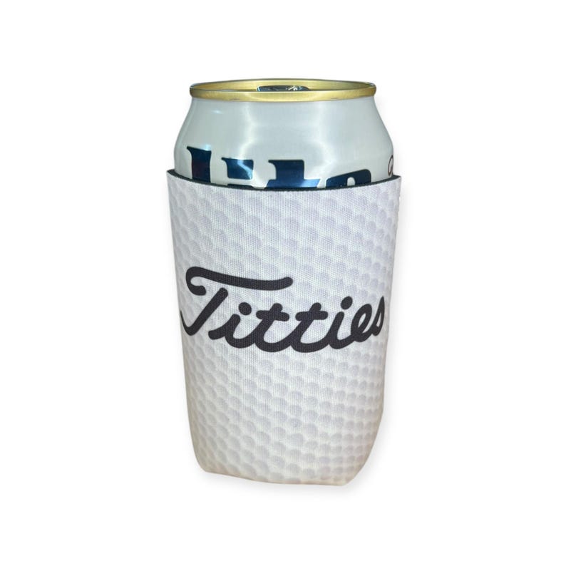 May include: White golf ball can cooler with black text that says "Titties".