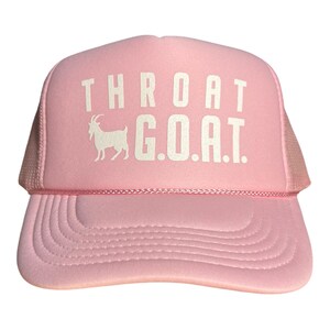 Pode incluir: Bon&eacute; de caminhoneiro rosa com tela branca nas costas. A parte frontal do bon&eacute; tem texto branco que diz "THROAT G.O.A.T." com uma silhueta branca de uma cabra.