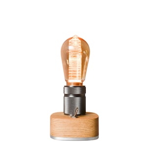 May include: A wooden table lamp with a vintage-style light bulb and a metal switch. The lamp is on a wooden base and has a warm, inviting glow.