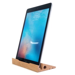Può includere: Un supporto in legno con finitura naturale tiene un tablet in orientamento verticale. Lo schermo del tablet mostra l'ora "14:28" e la data "Venerdì 14 ottobre".