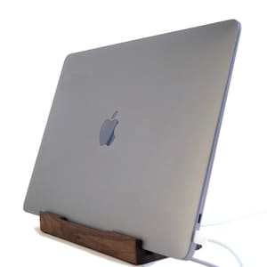 May include: A silver laptop computer is elevated on a wooden stand. The laptop is closed and the Apple logo is visible on the back.
