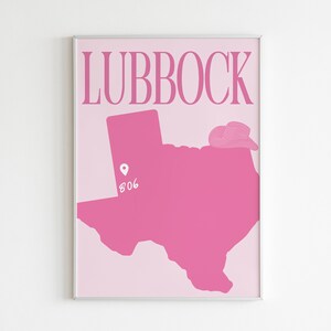 Pode incluir: Um p&ocirc;ster rosa com a palavra "LUBBOCK" em texto branco no topo. Um contorno rosa do estado do Texas est&aacute; abaixo do texto com um alfinete branco e o n&uacute;mero "806" dentro do contorno. Um chap&eacute;u de cowboy rosa est&aacute; no topo do contorno do Texas.