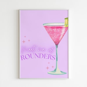 May include: A pink cocktail with a lime wedge in a martini glass on a light purple background with the text "Meet me at Rounders" in purple.