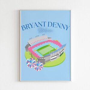 May include: A blue and pink illustration of Bryant Denny Stadium, home of the Alabama Crimson Tide football team. The stadium is surrounded by green grass and two blue and pink pom-poms.