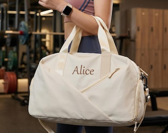 May include: Cream-colored duffel bag with the name "Alice" embroidered in brown. The bag has a zippered front pocket, a shoulder strap, and two top handles. The bag is designed for gym use.