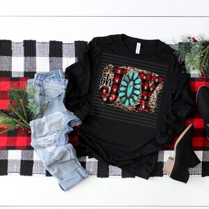 May include: Black long-sleeve shirt with a festive "Oh Joy" design featuring red and white plaid, turquoise, and leopard print. The design is embellished with rhinestones.