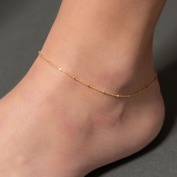 Op de afbeelding: Een delicate gouden enkelband met een simpel kettingontwerp. De enkelband is gemaakt van een dunne ketting met kleine, ronde kralen.
