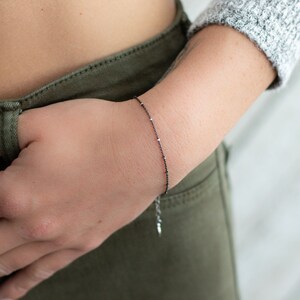 May include: A delicate black chain bracelet with small silver beads.