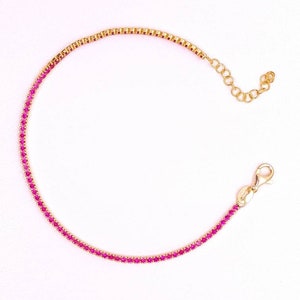 May include: A gold chain bracelet with pink gemstones. The bracelet has a lobster clasp closure.