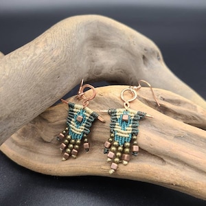 May include: A pair of green, beige, and copper earrings with a geometric pattern and copper beads hanging from the bottom.