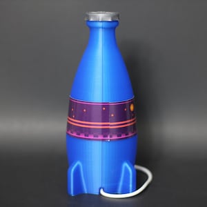 May include: A blue rocket-shaped bottle with a silver lid and a purple, orange, and white patterned label. The bottle has a white cord attached to the bottom.