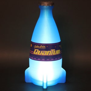 May include: A blue glass bottle shaped like a rocket with a white cap. The bottle has a label that says "Nuka Cola Quantum".