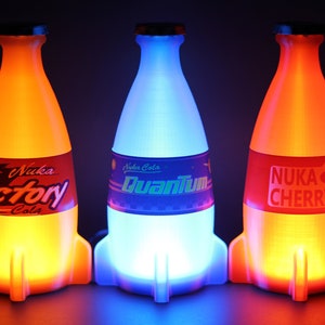 May include: Three glowing rocket-shaped bottles of Nuka Cola. The bottles are lit from within, with the left bottle glowing orange, the middle bottle glowing blue, and the right bottle glowing red. The bottles are labeled "Nuka Cola Victory", "Nuka Cola Quantum", and "Nuka Cola Cherry".
