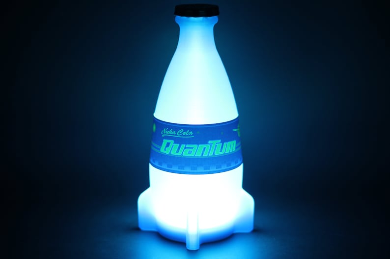 May include: A glowing blue Nuka Cola Quantum bottle with a rocket ship design. The bottle has a blue and green label with the text "Nuka Cola" and "Quantum".