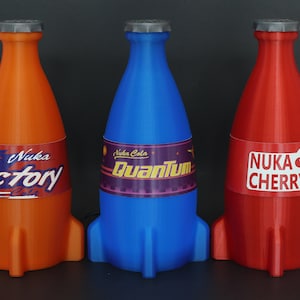 May include: Three rocket-shaped bottles of Nuka Cola, a fictional soda brand from the Fallout video game series. The bottles are orange, blue, and red, and each has a different flavor label: Victory, Quantum, and Cherry.