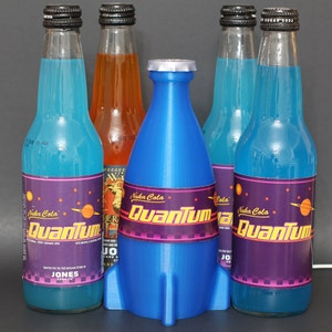 May include: Four glass bottles of blue and orange soda with a blue rocket-shaped bottle in the center. The bottles have labels with the text "Nuka Cola Quantum" and "Nuka Cola".