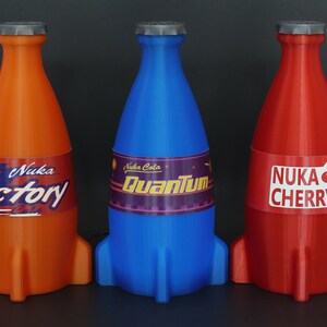 May include: Three rocket-shaped bottles of Nuka Cola, a fictional soda brand from the Fallout video game series. The bottles are orange, blue, and red, and each has a different flavor label: Victory, Quantum, and Cherry.