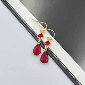 May include: A pair of gold earrings with red teardrop-shaped stones and smaller square red stones.