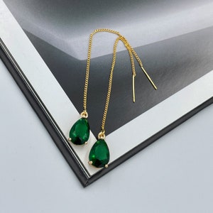 May include: Gold-tone threader earrings with teardrop-shaped, emerald green gemstones. The earrings feature a delicate chain and a simple bar at the end. The gemstones are faceted, catching the light and adding sparkle.