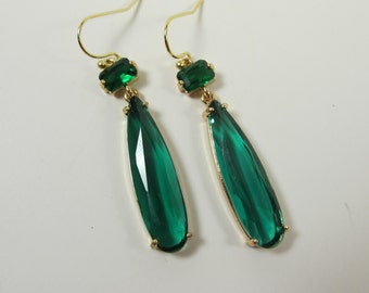 May include: A pair of gold dangle earrings with emerald green teardrop-shaped stones and smaller emerald green rectangular stones at the top.