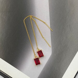 May include: A pair of gold chain earrings with red square-shaped gemstones hanging from the ends.