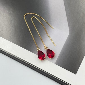 May include: A pair of gold dangle earrings with red teardrop-shaped crystals.