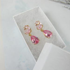 May include: A pair of pink teardrop earrings with gold settings. The earrings are displayed in a white box.
