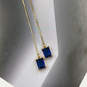 Puede incluir: Un par de pendientes de cadena dorada con piedras rectangulares azules.
