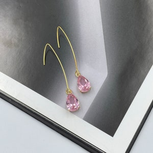 May include: A pair of gold dangle earrings with pink teardrop-shaped crystals.