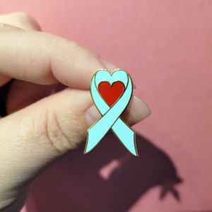 May include: A light blue ribbon with a red heart in the center. The ribbon is tied in a bow and is a symbol of support and awareness.